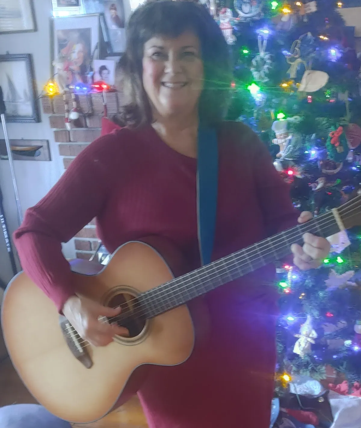 Kathy Lou playing acoustic guitar by a Christmas tree